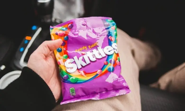 Person holding freeze-dried Skittles inside a car, showcasing vibrant colors and packaging.