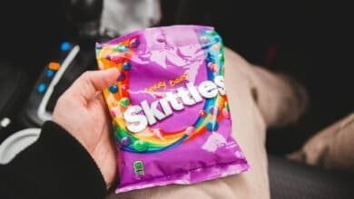 Person holding freeze-dried Skittles inside a car, showcasing vibrant colors and packaging.