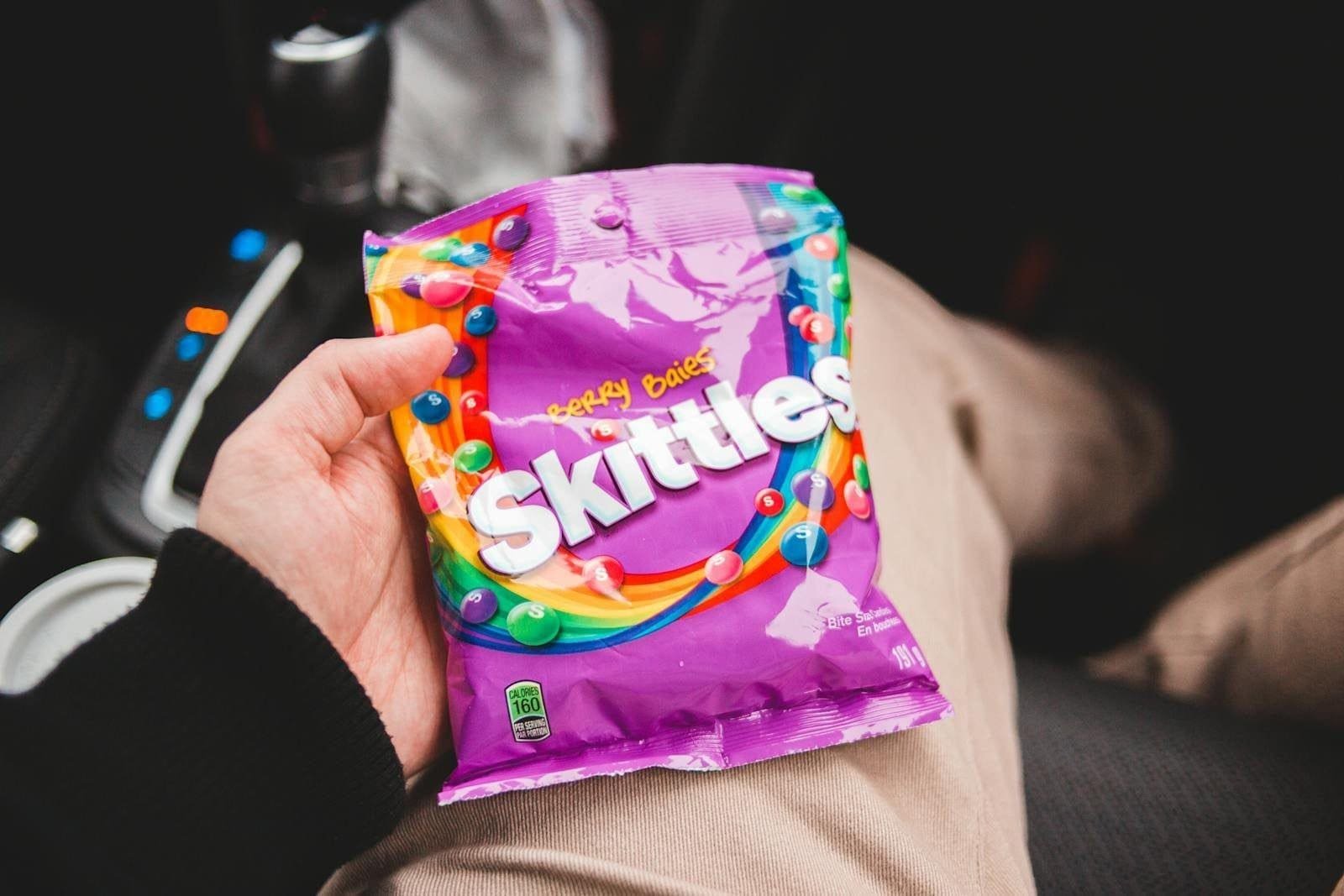 Person holding freeze-dried Skittles inside a car, showcasing vibrant colors and packaging.